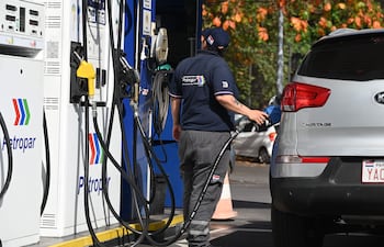 Empleado de Petropar en uniforme, sosteniendo una manguera de combustible frente a un Kia Sportage en una estación de servicio.