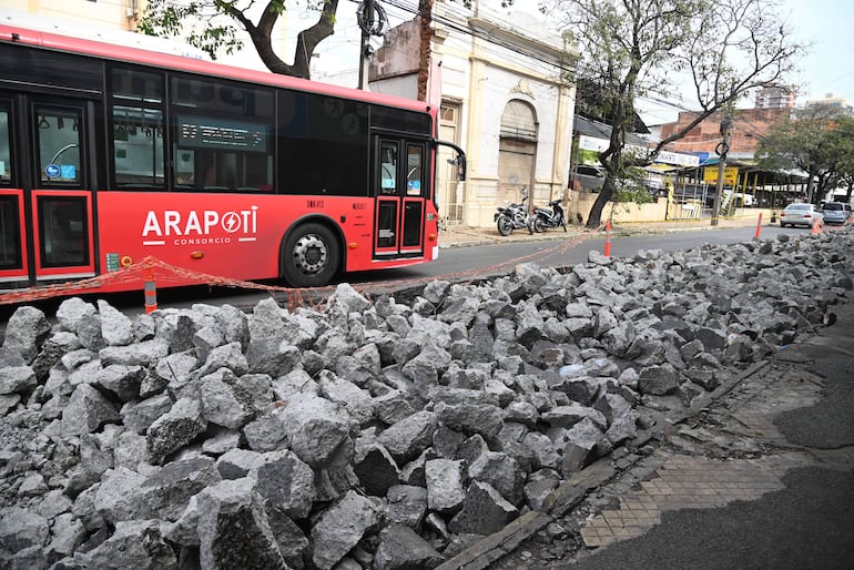 Autobús rojo del Consorcio Arapoty en calle con escombros, sin personas visibles, rodeado de vehículos estacionados.