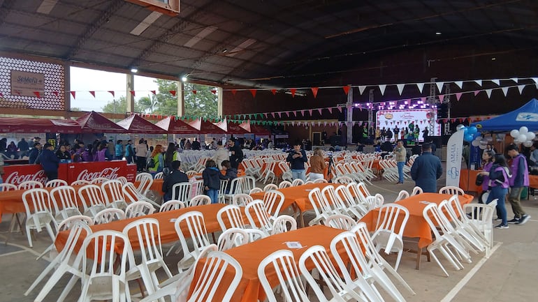 Ambiente festivo en la comilona de Teletón, con mesas decoradas y presencia de asistentes socializando entre stands de comida.