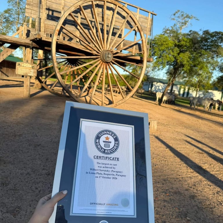 Certificado de Guinness en mano, con gran carro de madera y entorno natural de Loma Plata como fondo.