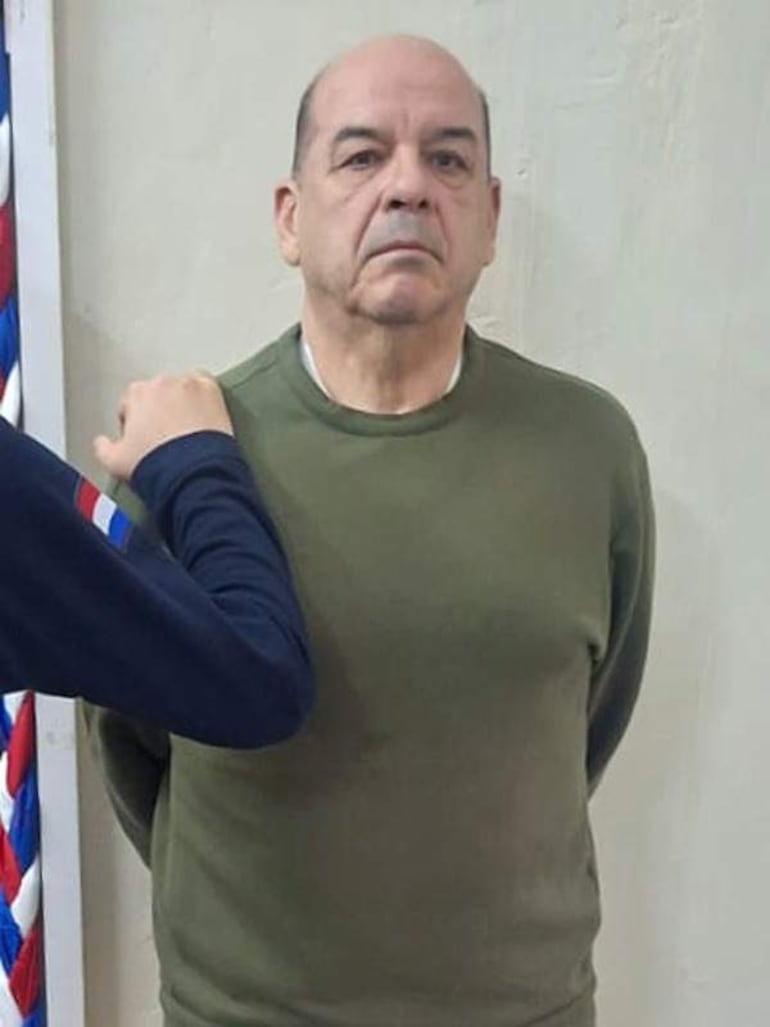 Miguel Ángel Robles de pie, con expresión seria y suéter verde oliva, mientras otro hombre lo toca levemente en el hombro.