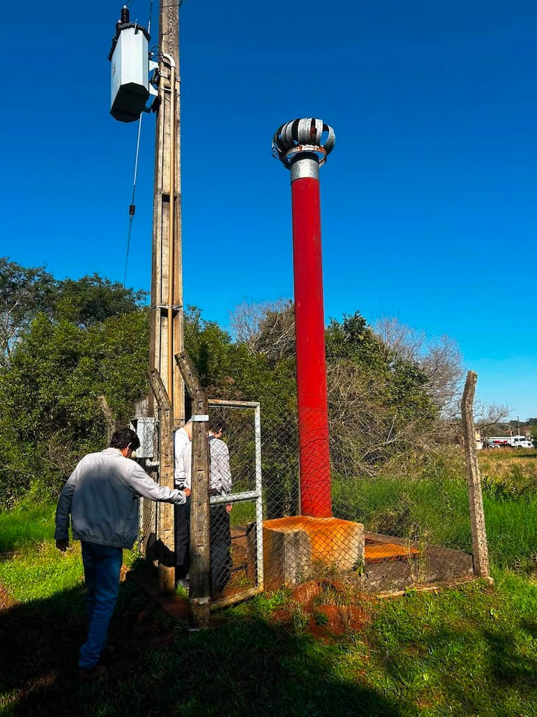 Dos hombres, uno de abrigo claro y otro de oscuro, inspeccionan una estructura de metal en un área verde bajo un cielo despejado.