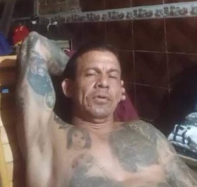 Hombre relajado y sentado con torso descubierto y tatuajes visibles en ambiente interior de vivienda común.