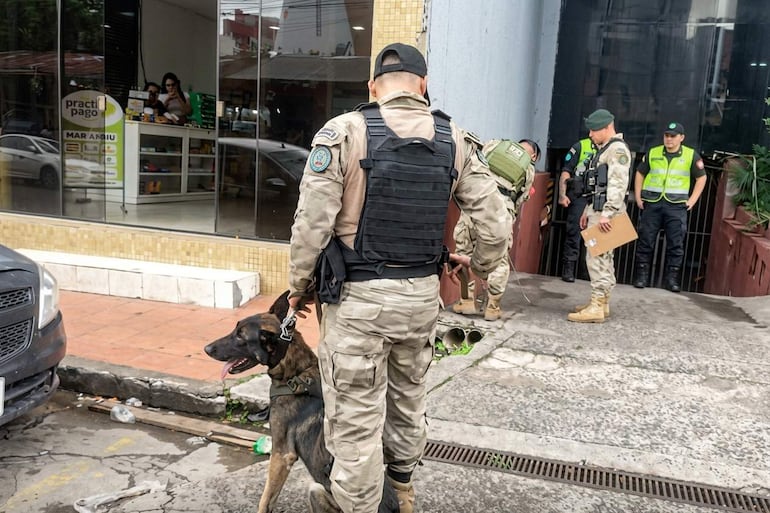 Seis personas con uniformes de seguridad en exteriores, un hombre sostiene un perro, mientras otros observan documentos.