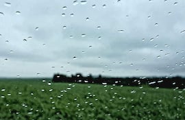 Cristal con gotas de agua en primer plano, con un fondo de paisaje verde y cielo nublado.