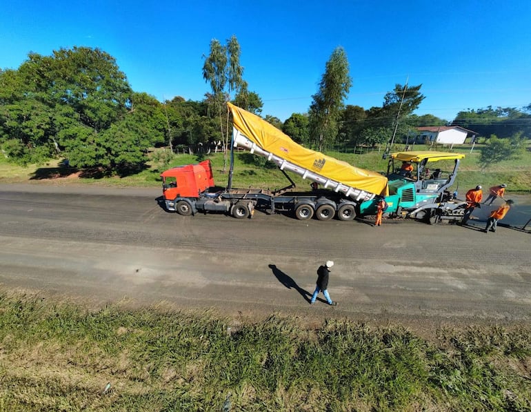 Cinco operarios en overoles naranjas y sombreros trabajan en la carretera, junto a un camión rojo y maquinaria de construcción.