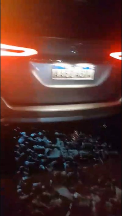 Parte trasera de una camioneta plateada detenida, con luces traseras encendidas, en un entorno oscuro.