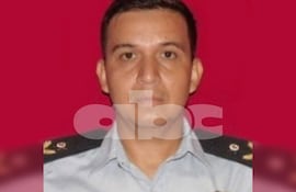 Hombre en uniforme azul claro con epaulettes, mirando hacia la cámara frente a un fondo rojo, sin otras personas visibles.