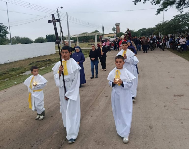 Tres niños con túnicas blancas y cintas amarillas, uno sostiene una cruz y otro una vela, durante la procesión en Puerto Sastre.