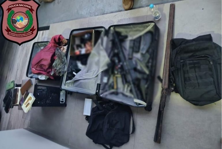 Dos maletas abiertas con ropa, un arma militar y objetos personales en un entorno de intervención policial.