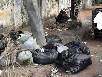 Acumulación de bolsas de basura en la acera en un entorno urbano desolado, con paredes grafiteadas y sin personas presentes.