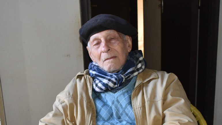 Sixto Sosa Ramírez, hombre mayor de 95 años, con abrigo claro y bufanda azul y blanca, sentado con expresión tranquila.