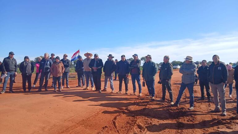 Grupo de personas con ropa abrigada y gorras, una bandera de Paraguay ondeando al fondo, sobre un terreno rojo.
