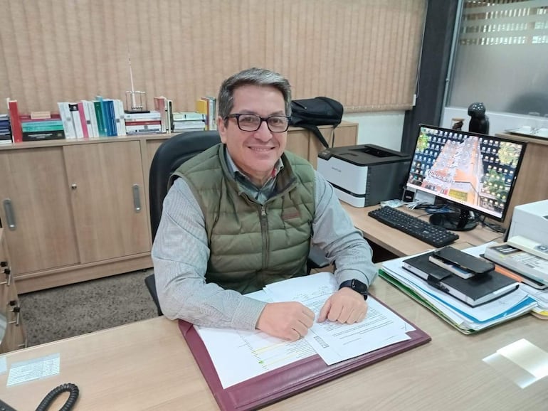 Christian Ruíz Díaz, con chaleco verde y camisa de cuadros, sonríe en su oficina rodeado de libros y objetos de trabajo.