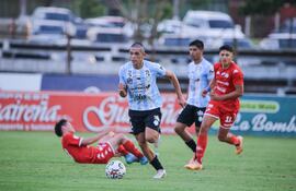 Patricio Coronel escapa en velocidad luego de recuperar el balón de los pies del defensor de Nacional Carlos Espínola, quien se encuentra en el suelo.