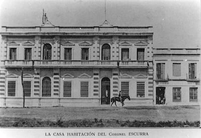 Hombre montado a caballo frente a un edificio clásico, con césped y un entorno urbano visible.