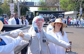 Hombres y mujeres con camisetas blancas y banderas participan en una manifestación, destacando un muñeco y una sombrero grande.