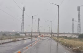 Vista de carretera lluviosa que lleva a un estadio, sin personas presentes y con ambiente gris y nublado.