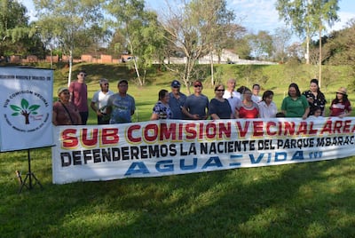 Grupo de 15 personas de pie y sentadas frente a un banner sobre la defensa del parque Mbaracayú, en un entorno verde.