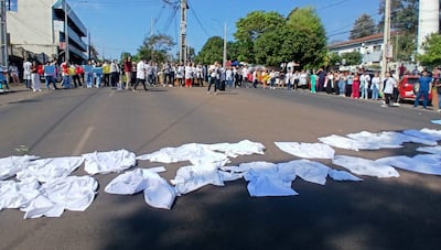 Médicos con batas blancas en la calle, sosteniendo carteles y globos, algunas camisetas esparcidas sobre el asfalto.