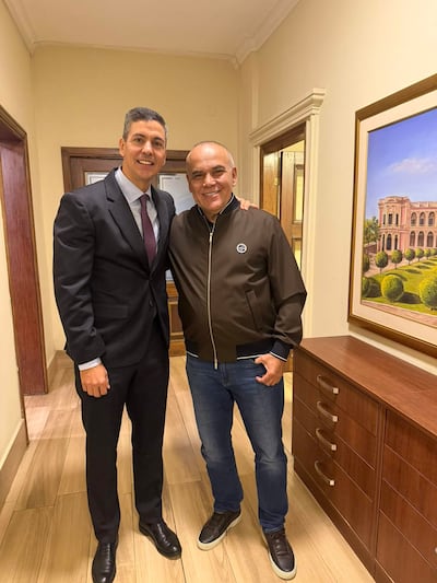 Peña y Nüñez sonríen en una oficina, Peña con traje negro y Nüñez con chaqueta marrón y jeans.