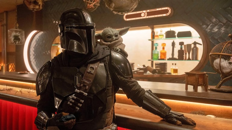 Personaje con casco y armadura oscura en un bar, sosteniendo un objeto mientras una criatura lo observa con grandes ojos.