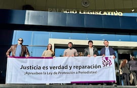Cinco personas, cuatro hombres y una mujer, sostienen un banner enérgico en la protesta frente al Congreso, con el Palacio Legislativo al fondo.