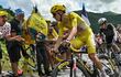Ciclista en maillot amarillo en carrera, mientras espectadores animan con carteles en ambiente soleado y montañoso.