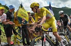 Ciclista en maillot amarillo en carrera, mientras espectadores animan con carteles en ambiente soleado y montañoso.