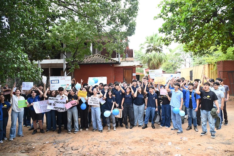 Estudiantes del CTN sosteniendo carteles con mensajes de protesta, expresiones de entusiasmo, al aire libre con árboles y edificio de fondo.