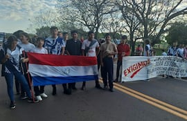 Jóvenes con camisetas variadas sostienen pancartas en la ruta, visiblemente comprometidos en su protesta por derechos educativos.