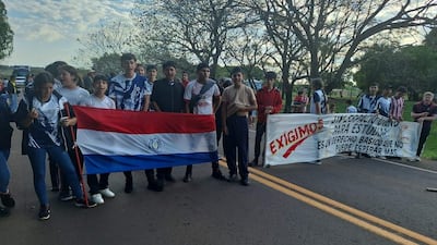 Jóvenes con camisetas variadas sostienen pancartas en la ruta, visiblemente comprometidos en su protesta por derechos educativos.