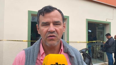 Jorge Vidallet, con camisa a cuadros rojos y chaleco gris, habla a la cámara sosteniendo un micrófono de prensa.