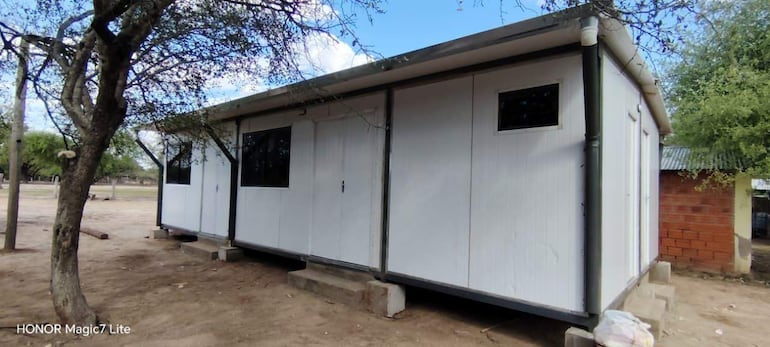 Estructura modular blanca con detalles grises, en un entorno rural tranquilo y arbolado, sin personas visibles.