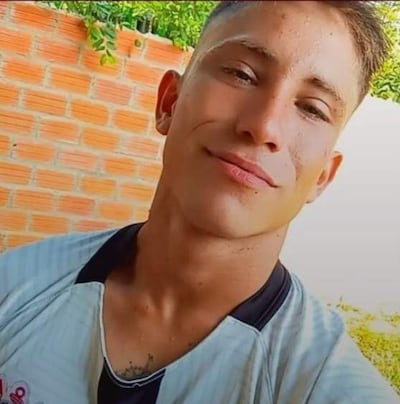 Emilio Ferreira Garay, hombre de tez clara con camiseta blanca, posa en un patio con fondo de ladrillos y plantas.