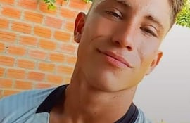 Emilio Ferreira Garay, hombre de tez clara con camiseta blanca, posa en un patio con fondo de ladrillos y plantas.