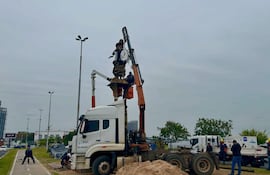 Cinco trabajadores, tres en un camión y uno con pala, manipulan una estatua elevada por un brazo mecánico en la Costanera.