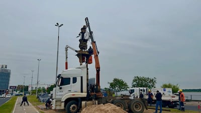 Cinco trabajadores, tres en un camión y uno con pala, manipulan una estatua elevada por un brazo mecánico en la Costanera.