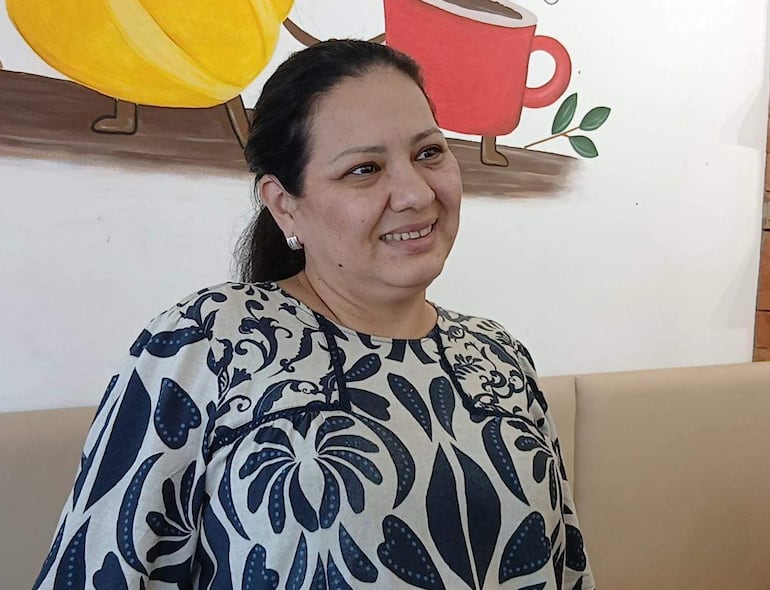 Ana Karajallo, mujer sonriente con blusa estampada, sentada en un ambiente acogedor con decoración de café.