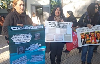 Dos mujeres sostienen carteles con mensajes de protesta en un acto frente al Palacio de Justicia, rodeadas de otros manifestantes.