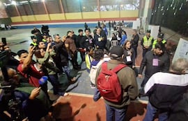 Grupo de personas en un gimnasio, algunos documentan la situación con móviles. Un hombre con mochila roja y chaqueta oscura en el centro de la conversación.
