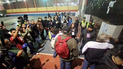 Grupo de personas en un gimnasio, algunos documentan la situación con móviles. Un hombre con mochila roja y chaqueta oscura en el centro de la conversación.
