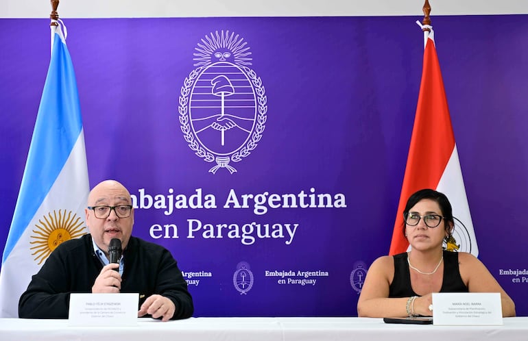 Maria Noel Ibarra y Pablo Felix Staszewski en conferencia, ambos con gafas, discutiendo frente a una mesa blanca y las banderas de Argentina y Paraguay.