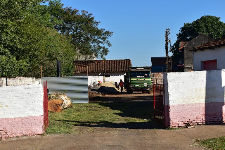 Dos trabajadores, uno con chaleco naranja, manipulando materiales en un terreno de construcción con un camión Scania al fondo.