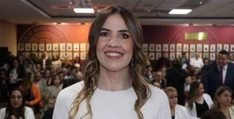 Andrea Soledad Ríos Dos Santos sonríe, vestida con blusa blanca, en un evento formal con personas en vestimenta de gala.