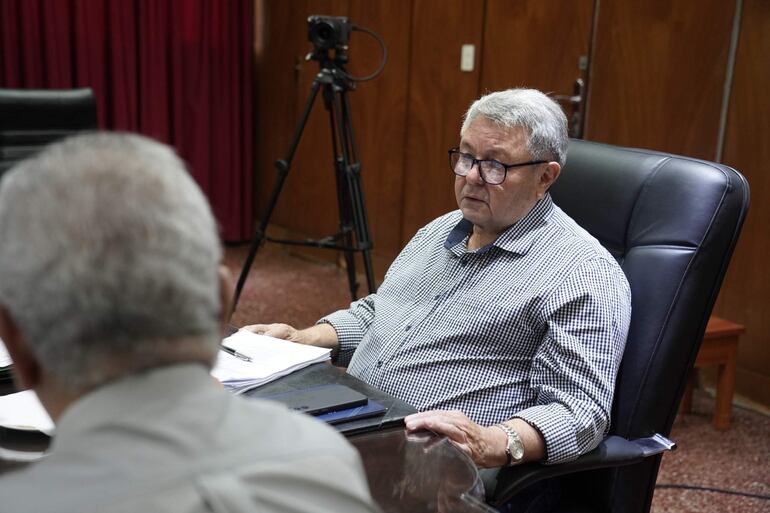 Víctor Insfrán Dietrich, con camisa a rayas y gafas, sostiene documentos mientras discute en un ambiente formal.