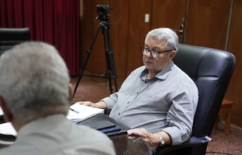 Víctor Insfrán Dietrich, con camisa a rayas y gafas, sostiene documentos mientras discute en un ambiente formal.