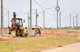 Tres trabajadores en casco amarillo y chalecos reflectantes en un sitio de construcción, uno opera un excavador.