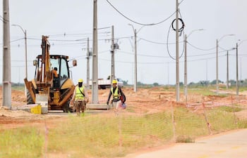 Tres trabajadores en casco amarillo y chalecos reflectantes en un sitio de construcción, uno opera un excavador.