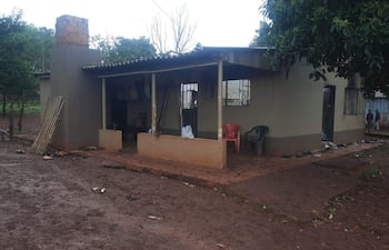 Casa de un solo piso con columnas en la entrada, sillas plásticas de colores, en un entorno rural y húmedo.